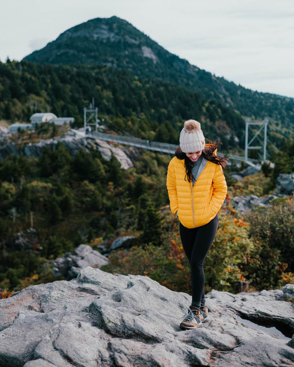 Woman in yellow jacket with the Mile High Swinging Bridge at Grandfather Mountain in the background