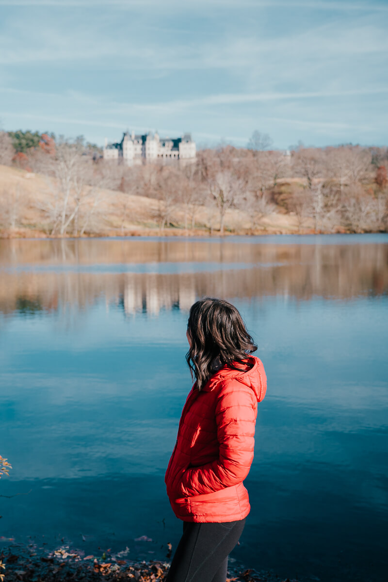 Woman in red jacket standing at Biltmore Lagoon Lookout with Biltmore House in the background