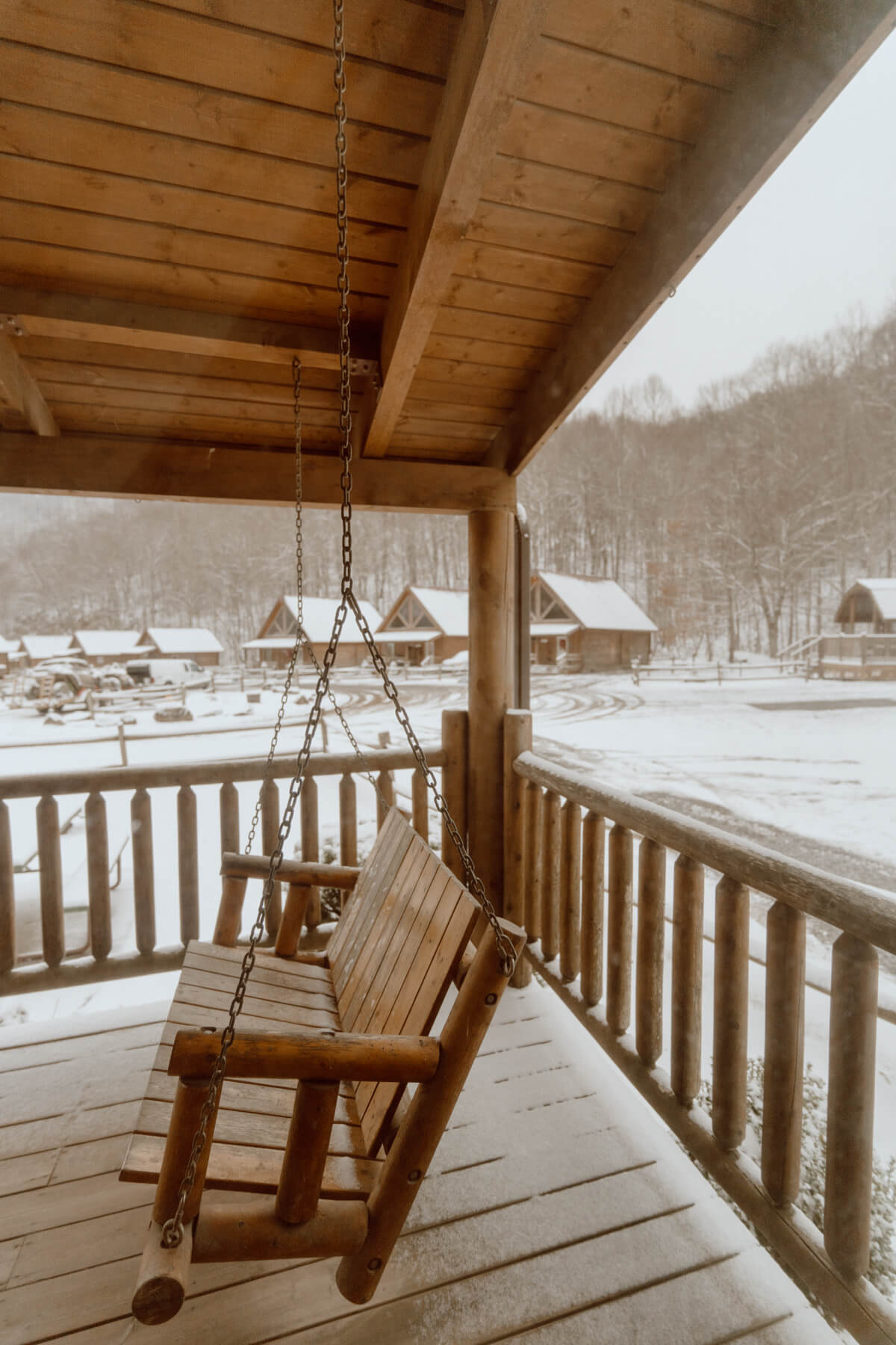 Close up of log cabin front porch swing with snow covered cabins in the distance
