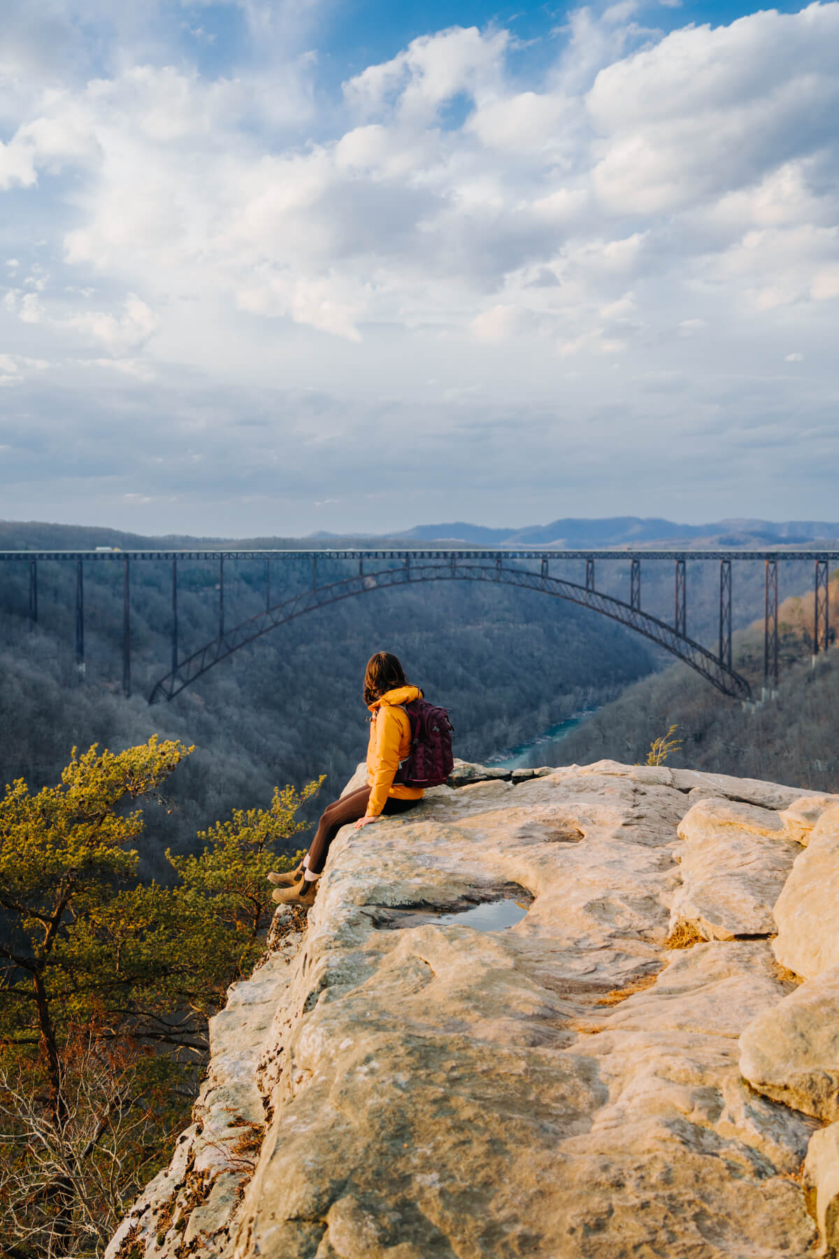 Woman sitting on rock outcropping with New River Gorge Bridge in the distance 