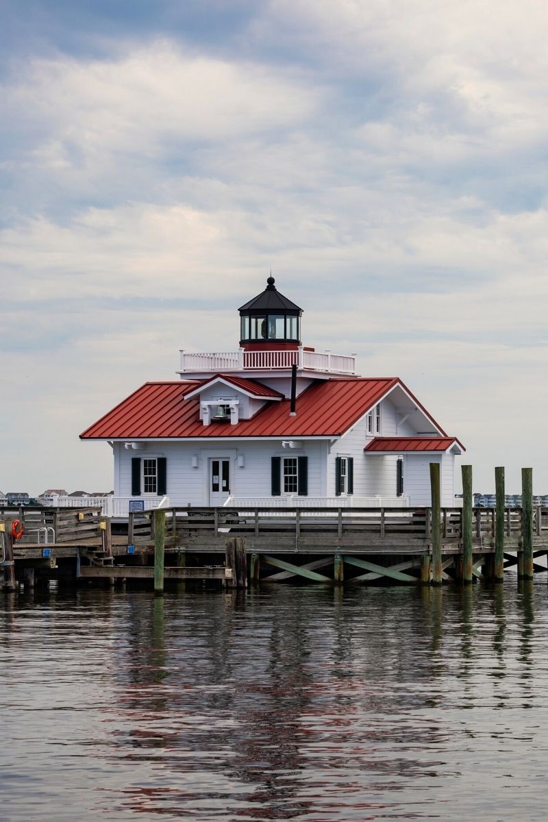 Small, coastal lighthouse with a red metal roof on the water