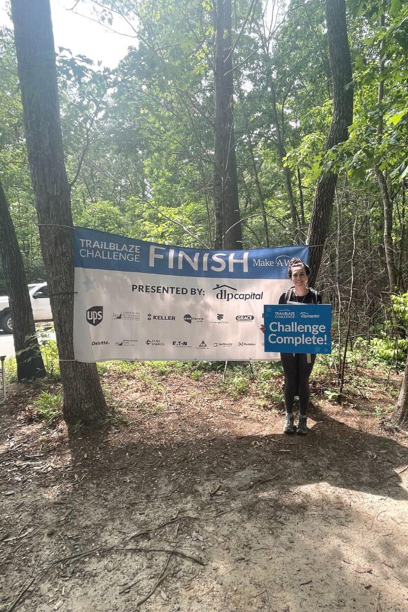 Hiker holding "Challenge Complete" sign at the Trailblaze Challenge finish line